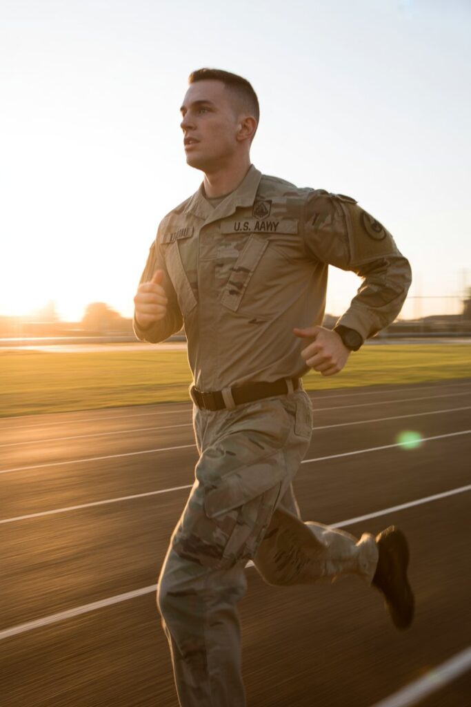 A U.S. Army soldier in PT uniform running on a track at sunrise, motion blur on legs, determined expression, golden hour lighting, cinematic wide shot, photorealistic

